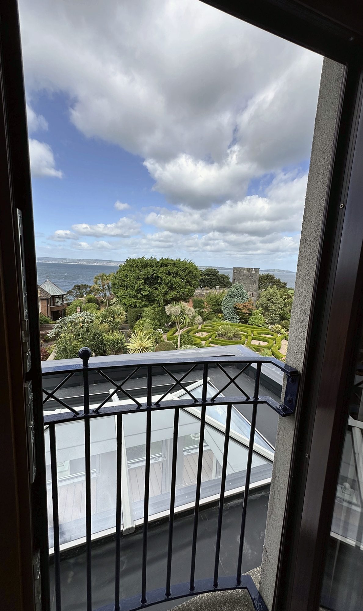 View from an upper window over the roof lantern to gardens, a tower and the sea