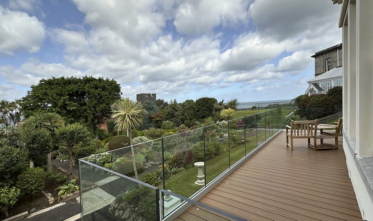 Composite deck terrace with glass balustrade overlooking gardens and the sea