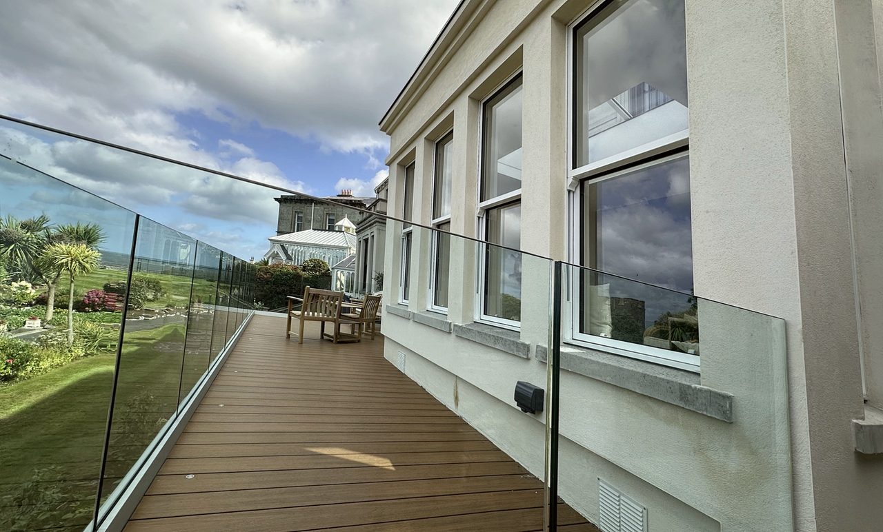 Composite deck terrace with glass balustrade running along the rendered side wall of the house