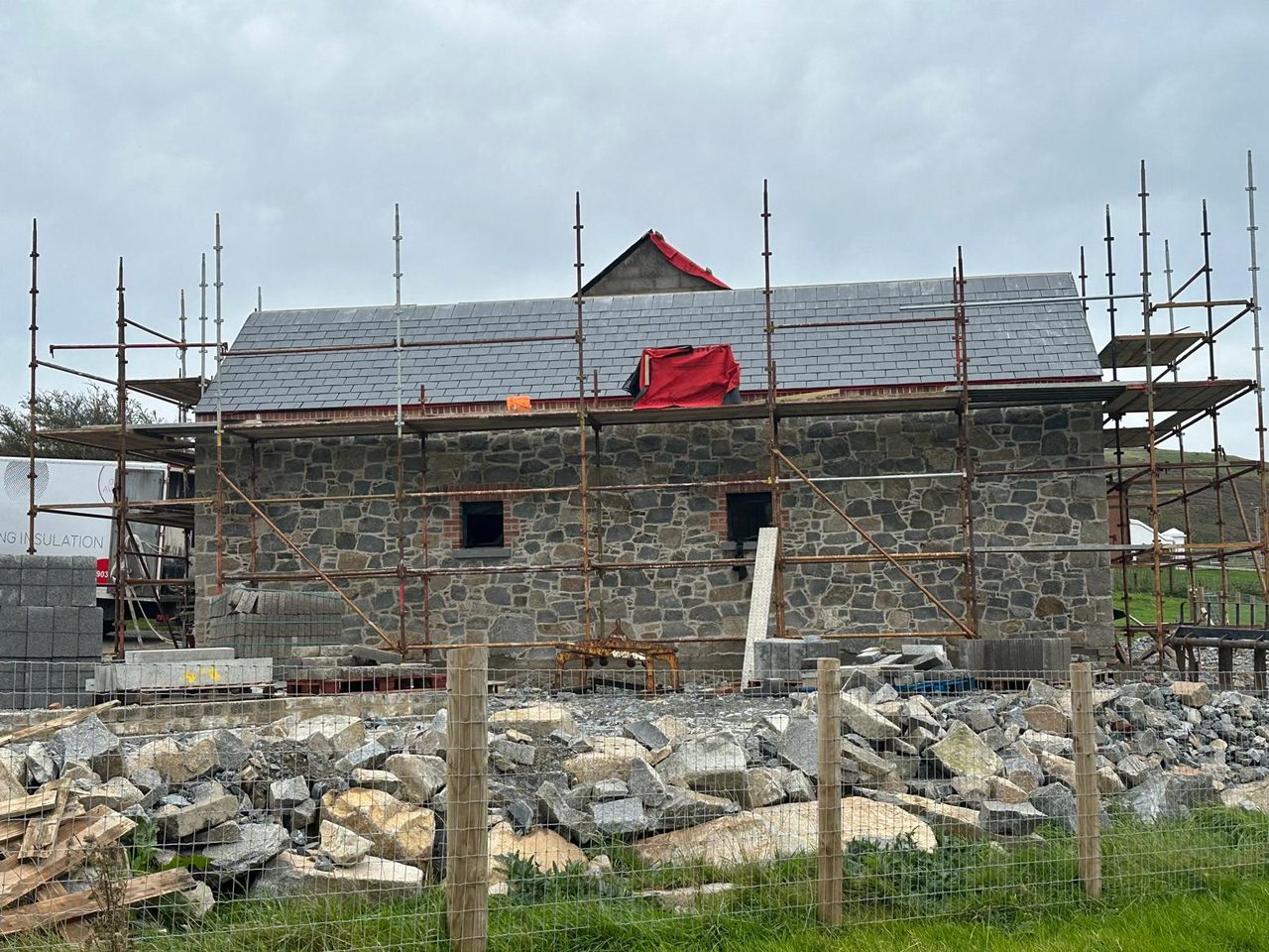 Natural stone elevation with a slate roof, scaffolding and a pile of stone in front